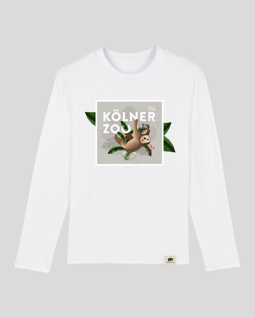 Weißes Langarmshirt mit quadratischem Frontprint: Ein gezeichnetes Faultier hängt an einem Ast, umgeben von grünen Blättern und roten Beeren. Darüber steht in weißen Großbuchstaben ‚Kölner Zoo – seit 1860‘. Am unteren Saum ist ein kleines Label mit Elefantenlogo eingenäht.